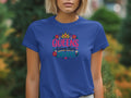 A woman wearing a blue t-shirt printed with the text QUEENS living their DREAMS, framed by a crown and flowers.