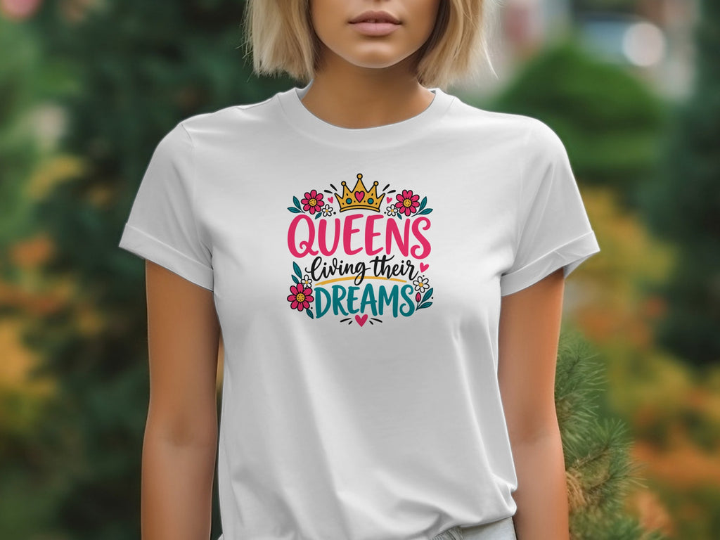 A person wearing a white t-shirt featuring the graphic text Queens living their dreams surrounded by flowers and a crown.